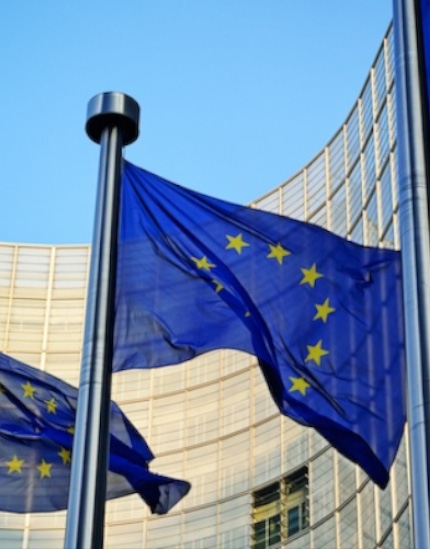 Bandeiras da união europeia hasteadas com um prédio espelhado ao fundo